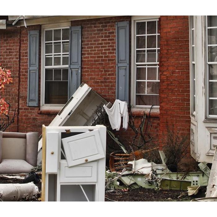 damaged furniture and other home items sitting outside of red brick house 