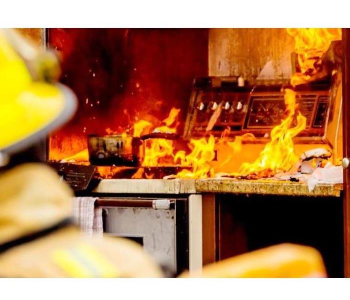 "Blurry firefighters back with a sharp image of a restaurant kitchen stove with an open flame on top" 