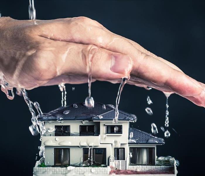 "Image of a wet hand dripping water over a small model home with a black background" 
