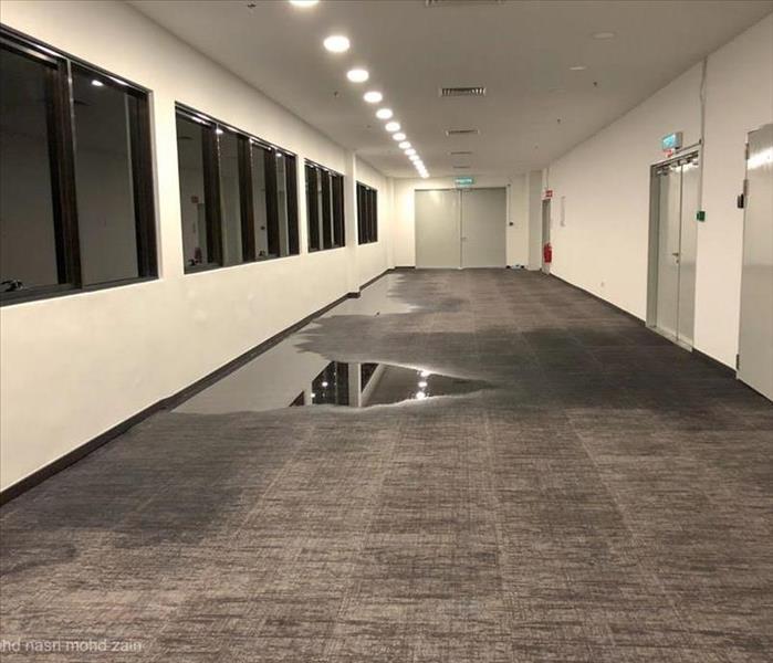 "large hallway of a commercial building with flooding down the left side of hallway underneath black windowsn"